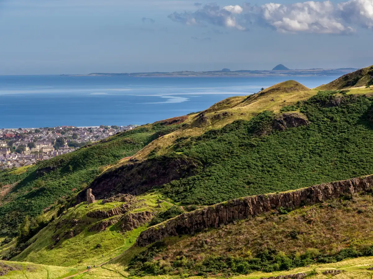 Walkers on the grassy flank of Arthur's Seat above Edinburgh, the city spread out below